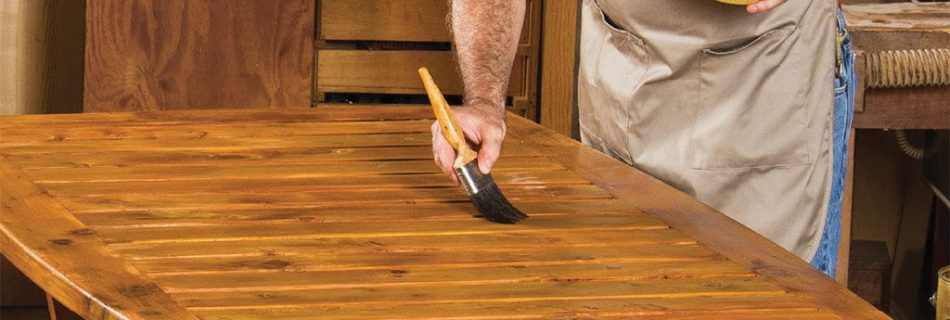 A professional woodworker applying a smooth, clear protective finish onto a custom hardwood tabletop using a clean brush.