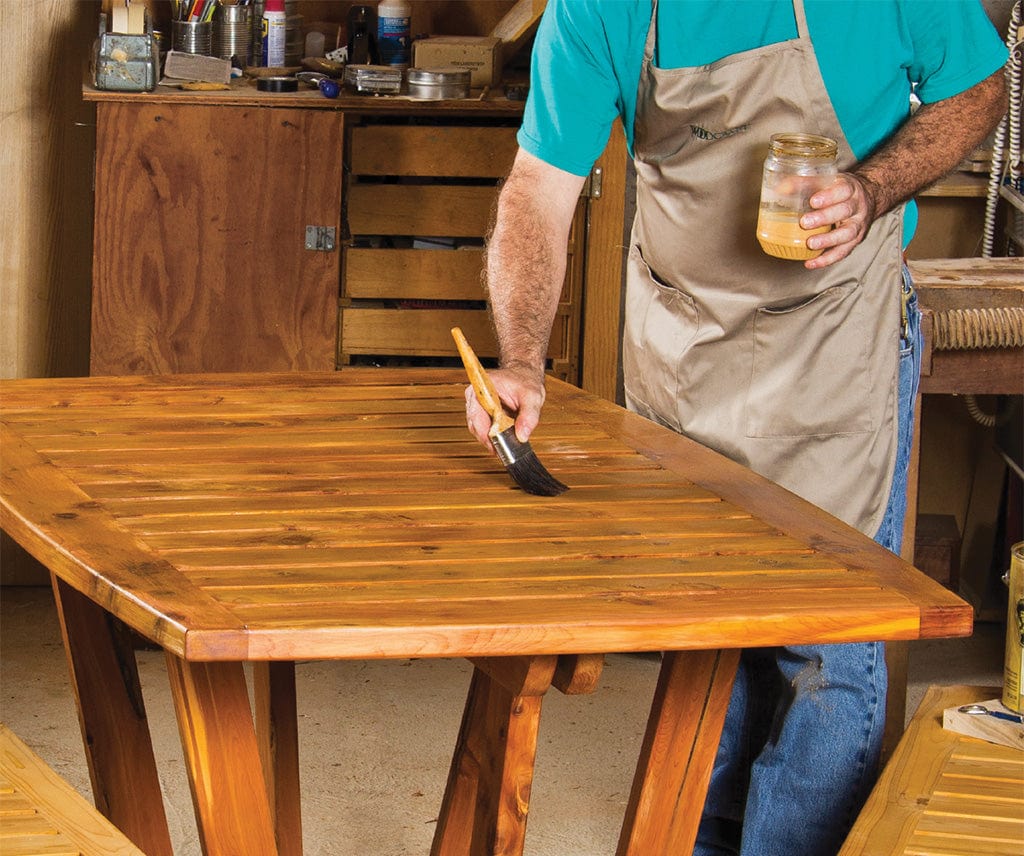 A professional woodworker applying a smooth, clear protective finish onto a custom hardwood tabletop using a clean brush.